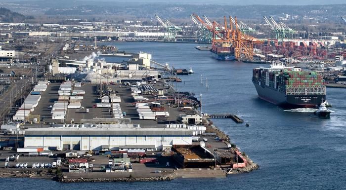 An aerial view of shipping containers stacked in a terminal and large cargo vessels docked at the Port of Tacoma, representing the scale of maritime logistics and industrial site protection.