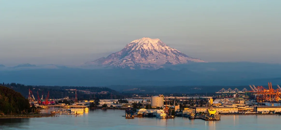 An aerial view of the Port of Tacoma with Mount Rainier in the background, representing a major industrial service area for On-site Security Officers and Patrol Services in the City of Tacoma.