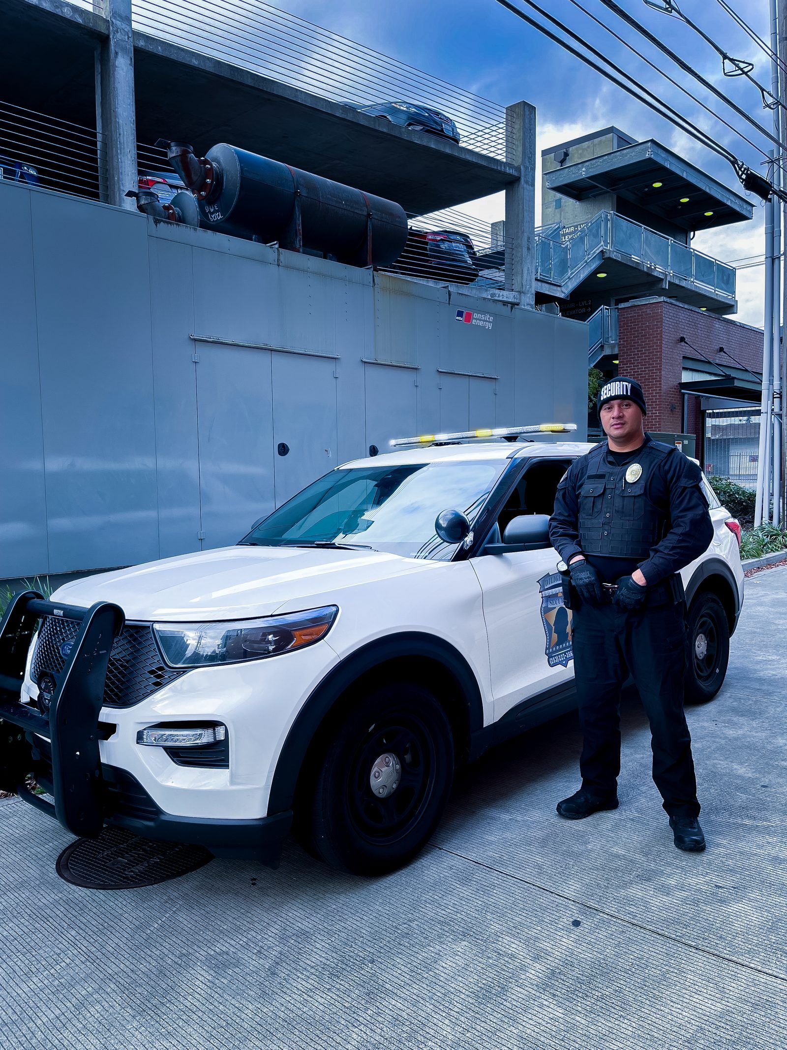 A Diligence Security Patrol Officer standing beside a marked patrol vehicle inside a commercial parking structure