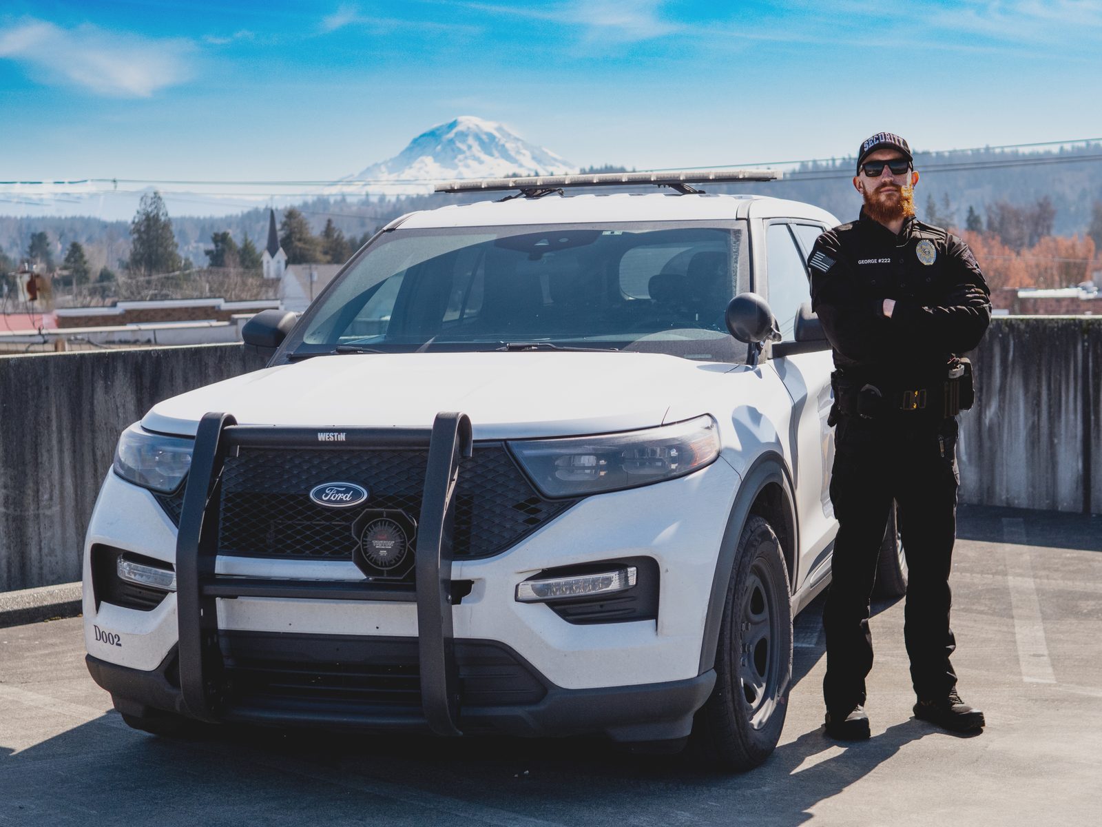 Professional Diligence Security Officer in full uniform standing with a marked patrol vehicle and Mount Rainier in the background for visible deterrence
